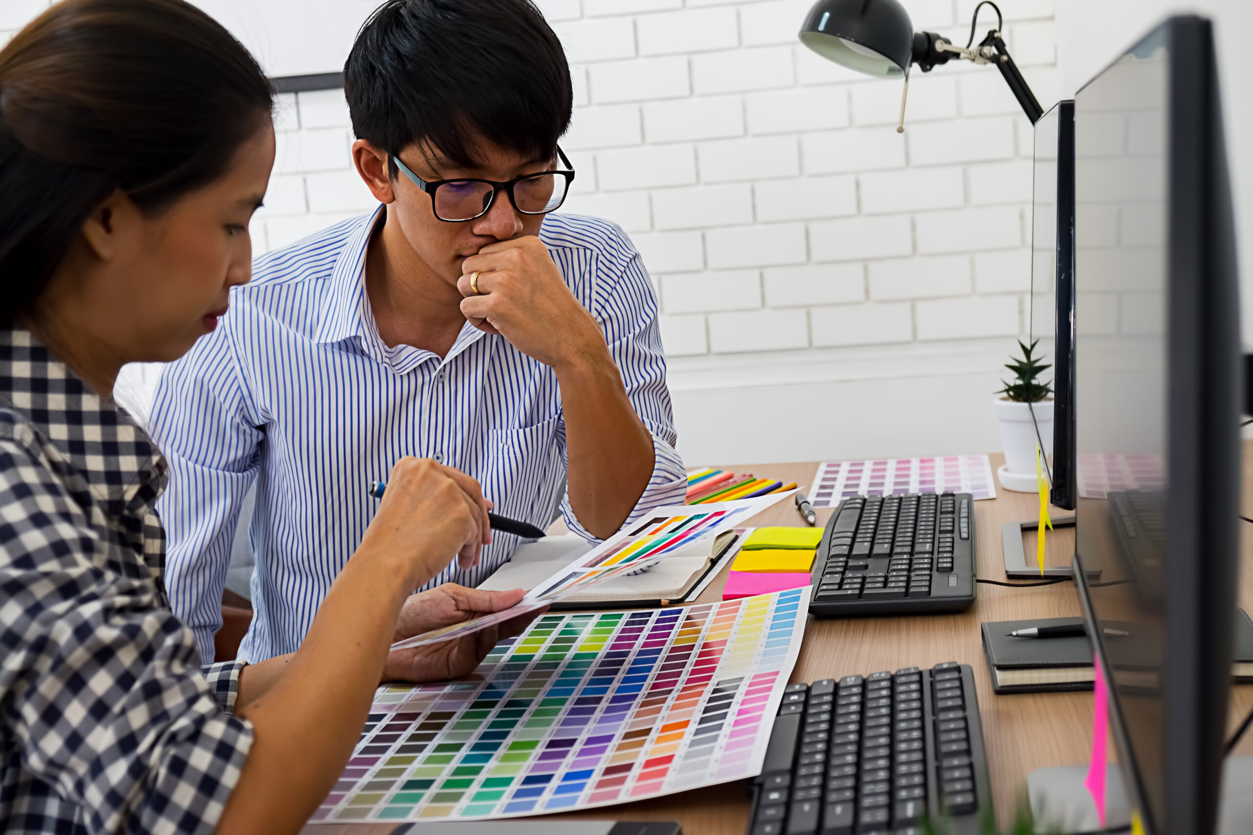 กราฟิกดีไซน์เนอร์กำลังเลือกสีจากสมุด PANTONE เพื่อใช้ในระบบพิมพ์ Offset ที่ต้องการความแม่นยำของสีแบรนด์และคุณภาพสีที่สม่ำเสมอ